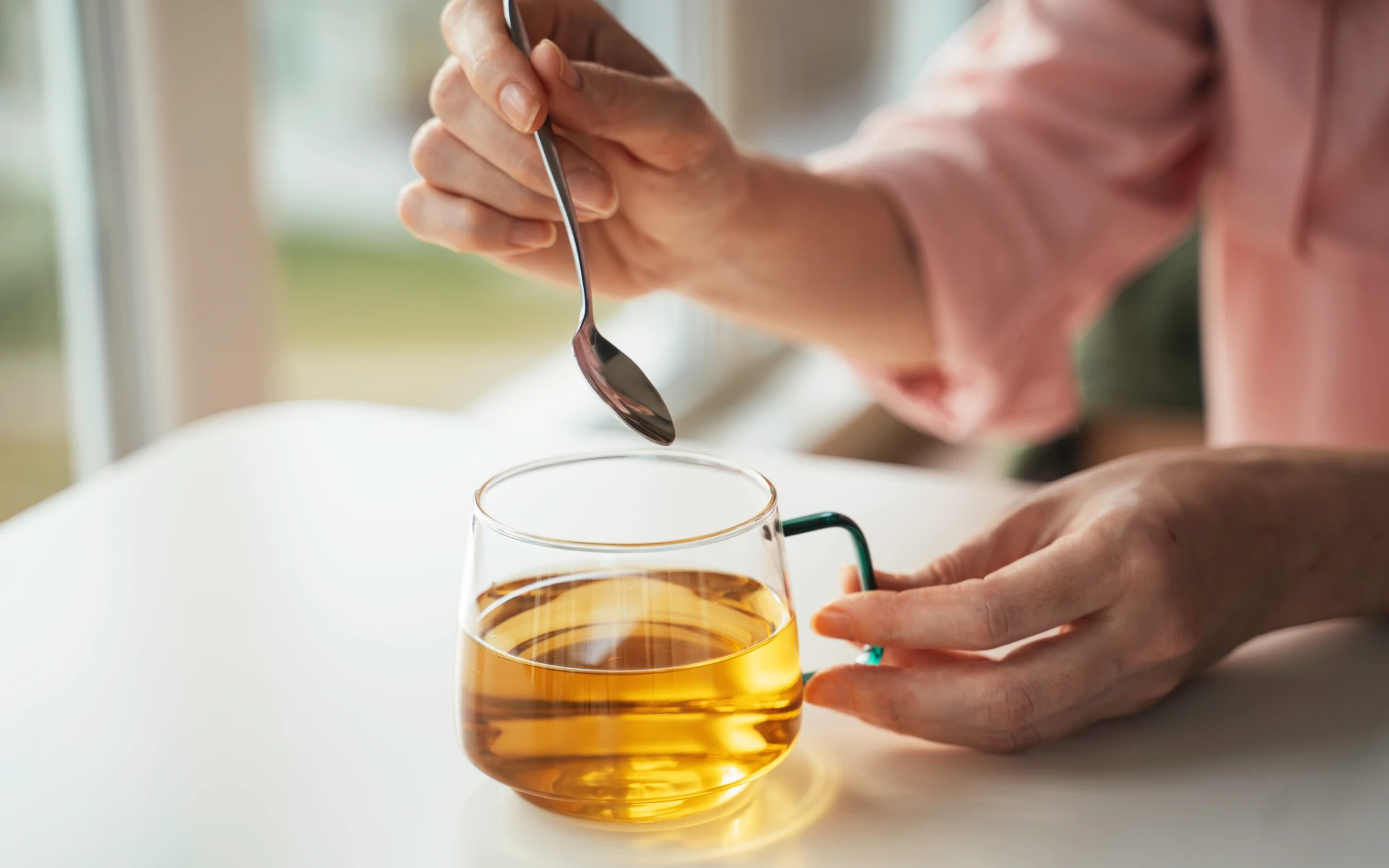 Person stirring tea in glass cup.